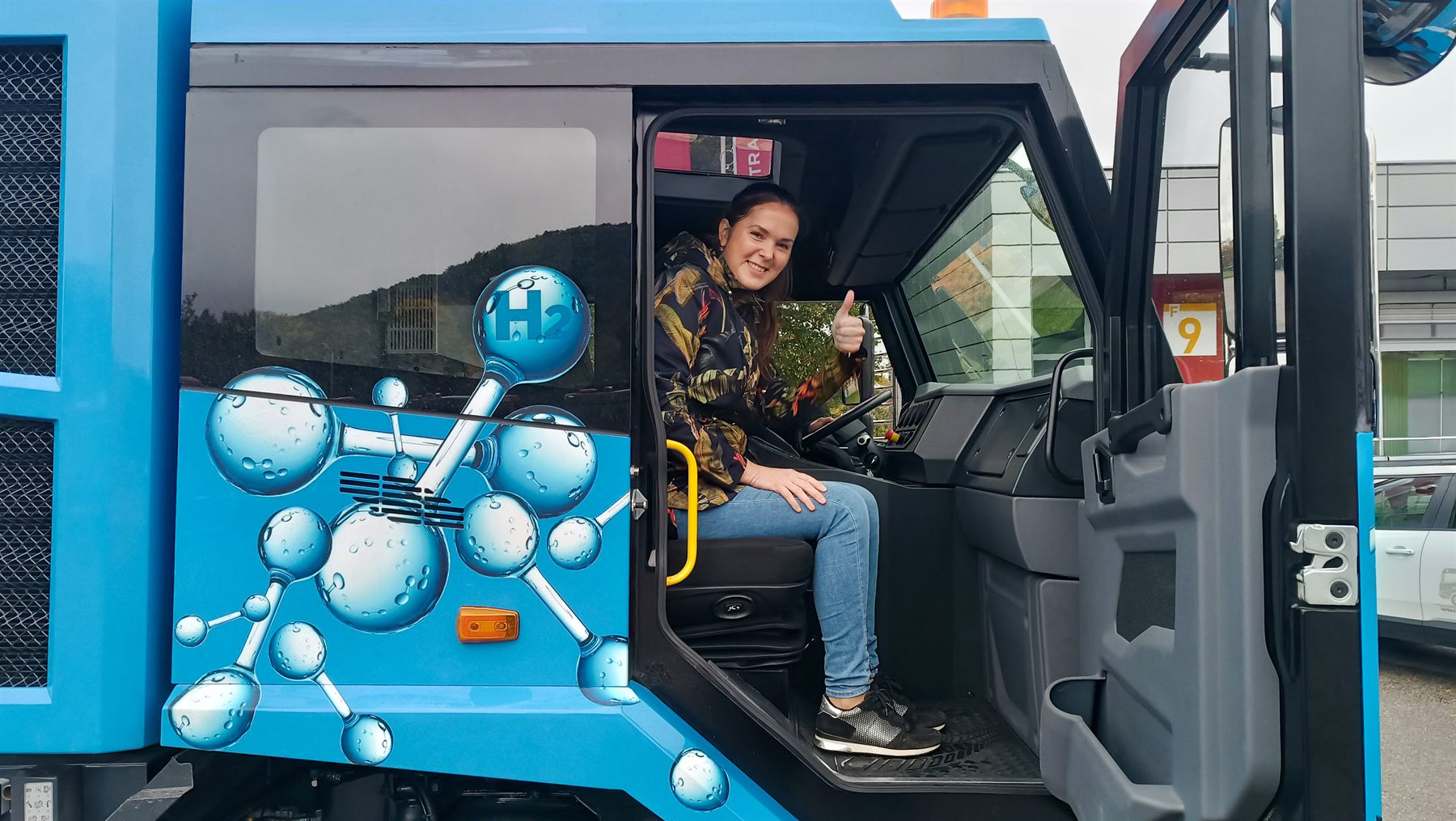 Řidič v kabině vodíkového nákladního vozidla TATRA s polepem molekuly vodíku.
